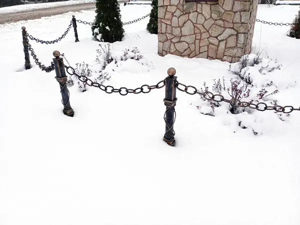 A metal chain link fence around a stone plinth in winter. A thick layer of snow covered everything around.
