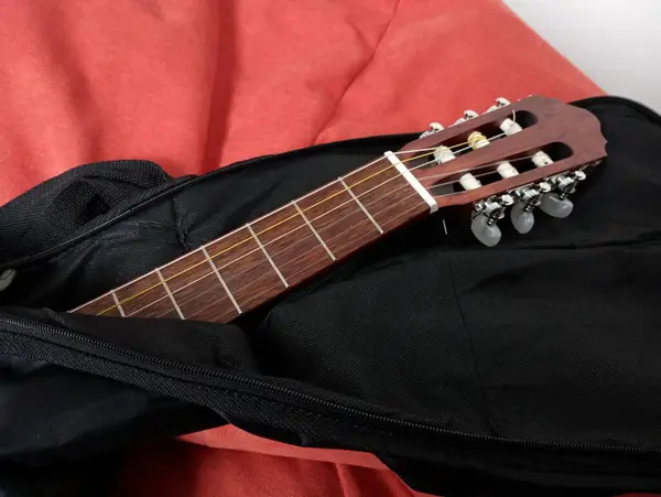 On a red soft chair made of a black cover looks like the neck of a guitar with stretched strings. The topic of music and musical instruments.