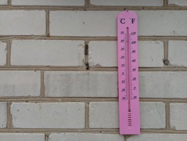 Pembe bir termometre eski beyaz bir tuğla duvara asılır. Dışarıdaki hava sıcaklığını ölçüyorum..