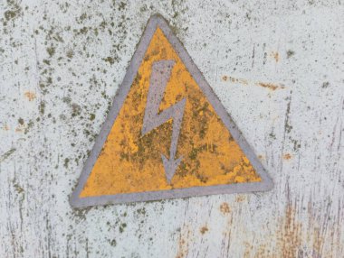 Üzerinde yıldırım olan sarı üçgen bir işaret, yüksek voltaj uyarısı yapan eski gri metal bir yüzeye boyanır..