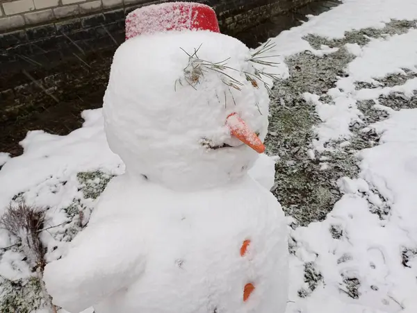 A snowman sculpture made of snow with a red bowl on his head and a carrot for his nose. Snow sculpture.