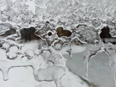 Eriyen ve bir kalıp oluşturan şeffaf soğuk buz dokusu. Buz kristalleri çatıdan sarkıyor. Gölün arka planında eriyen buz.