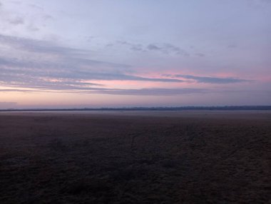 Gün batımı ufukta. Akşam gökyüzünün güzel manzarası. Çimenli bir alanda sisli bir akşam. Güneş ufukta batar ve gökyüzünü hafif bir ışıkla aydınlatır..