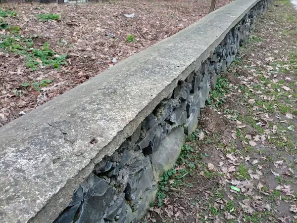 Stone and concrete fence. The old fence in the park is made of river black stone, the top of which is finished with concrete.