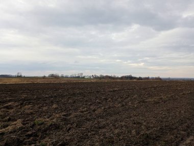 Tarıma elverişli arazi manzarası. Arazi kış için sürüldü. Ufukta bahar tarlaları, mavi gökyüzünün arka planında bir orman görülebilir. Bahar ve tarım temaları.