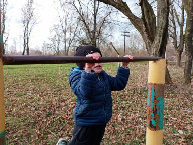 Altı yaşında küçük bir çocuk yatay çubukta egzersiz yapıyor. Çocuk sporları. Bir çocuk barfiks çekip barfiks çekiyor. Spor için metal çubuklar.