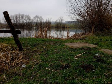 Güzel bir göl manzarası eski bir ahır ve kıyısında plastik çöpler bulunan eski ahşap bir çit. İnsan yaşamının ürünlerinin çevre kirliliği konusu.