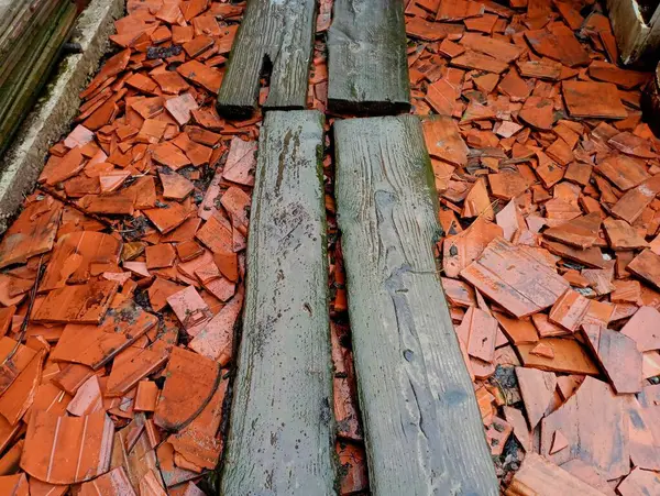 Wooden rotten boards on broken ceramic red roof tiles. Wet boards on construction waste. An impromptu passage on a pile of broken tiles with clapboards on a construction site.