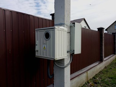 Elektrik tüketimini ve kullanımını ölçmek için elektrikli aletlerin saklandığı iki beyaz metal kutu. Metal bir çitin arka planında tezgahları olan özel kutular..