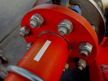 Boruların bağlantısı. Bir çemberdeki birçok cıvata kırmızı su sağlamak için boruları sıkıca birbirine bağlar. Tesisat ve su ikmali konuları. Kırmızı boru başka bir boruya bağlı ve daire içinde birçok cıvata var. Metal boruların hızlanması güvenilirdir..