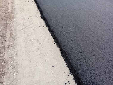 Fotoğrafı gri bir kaldırımla köşegen olarak ayıran yeni siyah, taze asfaltın arka planı.