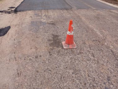 Yol kenarında eski asfalttan temizlenmiş turuncu bir trafik konisi. Onarımların yapıldığı yol at arabasının önünü kapatıyorlar..