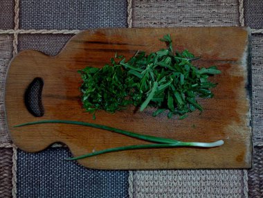 Sebze kesmek için kullanılan tahta bir tahtanın üzerinde yeşil soğan ve maydanoz var. Yemek ve baharatlar konusu. Sebze sağlıklı taze yiyecek..