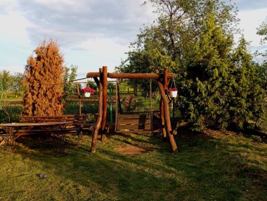 Bahçede sallanan, salıncağın kenarlarından sarkan ve gün batımında aydınlanan iki vazo çiçekli ahşap bir meşe ağacı. Bahçedeki evin yakınındaki tasarım ve dinlenme alanı..