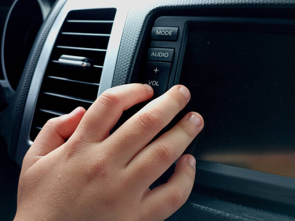 A person presses the volume down button on the multimedia device of the car with his finger. The topic of transport and comfort. Listening to music while driving.