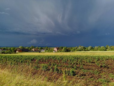 Köyün üstündeki parlak mavi bulutlu gökyüzü. Mavi gökyüzü ve parlak güneş ışığıyla fırtınadan önceki bir dönem. Ufuktaki büyük fırtına bulutları
