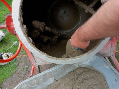 Bir insan, turuncu beton karışımından elle özel bir malayla beton kalıntıları seçer. İnşaat konusu. Beton karıştırıcıda betonun askıya alınması.