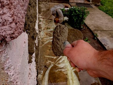 A person plasters a wall with a trowel, throwing concrete solution on a vertical wall. Construction process and repair. Man repairs walls. clipart