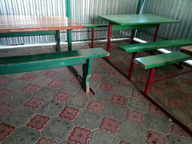 Binanın yakınındaki küçük bir kaldırım taşının üzerinde ahşap kaplı eski metal masalar. Eski köy dükkanının yakınında dinlenecek bir yer..