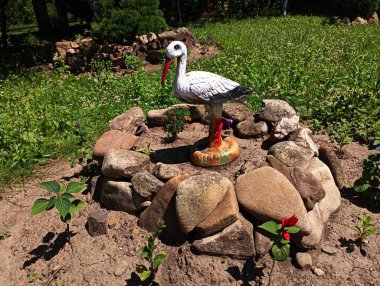 Topraktan ve çimenli yeşil bir çimenlikteki doğal taştan yapılmış taş bir çiçek tarhında beyaz bir leyleğin alçıdan heykeli..