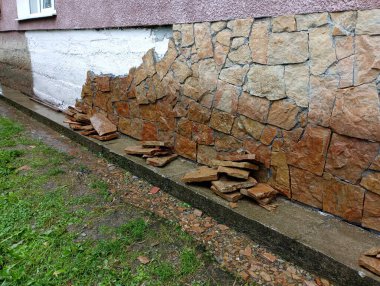 Kum taşı taşları, evin daha önce astar ile tedavi edilen beton temelinin kurulumu için evin duvarının yanına istiflenir. Onarım ve inşaat süreci.