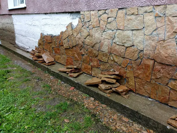 stock image Sandstone stones are stacked near the wall of the house for its installation on the concrete foundation of the house, which is previously treated with a primer. Repair and construction process.