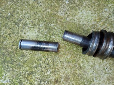 Eski beton arka planda kırık demir şaft. Bir traktör çim biçme makinesinin iki parçası..