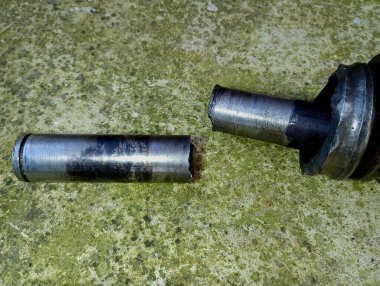 Beton, eski arka planda, yeşil renkli kırık bir metal şaft. Tarım makineleri için bozuk yedek parça. Ev aletlerinin bozulma konusu....