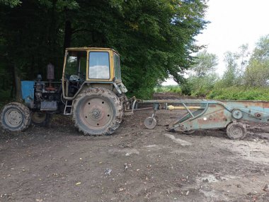 Patates kazı aletli bir traktör orman ağaçlarının gölgesine park edilmiştir. Sonbahar tarım işleri.