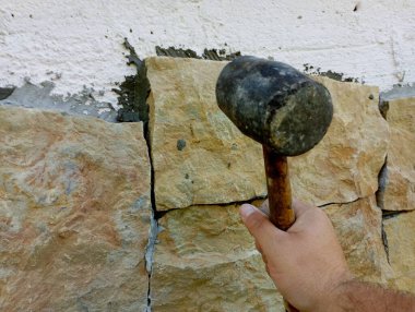 Evin dikey duvarına lastik çekiç gibi bir aletle doğal taşlar yerleştirmek..