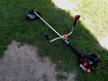 Dışarıdaki yeşil çimlerin üzerine siyah bir benzin çim biçme makinesi yerleştirilir. Çim biçme ve çimlerin bakımı konusu.