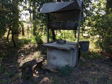 Bahçenin ortasında, beton halkalardan yapılmış uzun ağaçların gölgesinde metal çatılı ve yan tarafına kova bağlanmış eski bir resim kuyusu. Köydeki su kaynağı. Eski köy..