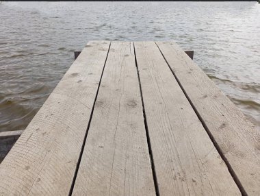 Gölün üzerindeki ahşap platform. Balıkçılık ve eğlence teması. Suyla arka plan ve su üzerinde küçük dalgalarla ahşap köprü.