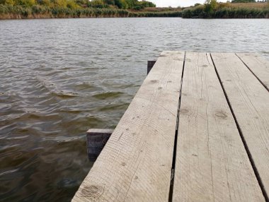 Temiz suyla sıcacık bir gölette manzara. Rezervuardaki ahşap iskeleden görüntü. Sonbaharda resimli doğa.