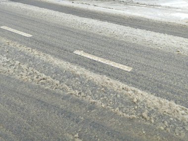 Yol yüzeyinde eriyen karların içinden çıkan beyaz işaretler var. Buzlar çözülürken asfalt yol yüzeyi.