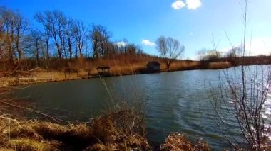 Temiz suyu olan sonbahar gölü ve kıyılarda balık tutmak ve dinlenmek için küçük ahşap evler. Hafif bir rüzgar su yüzeyinde küçük dalgalar yaratır.