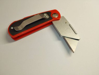 Kırmızı inşaat bıçağı, beyaz arka planda yarı katlanmış bir pozisyonda. Beyaz arka planda inşaat aracı. Kırtasiye bıçağı. Keskin bıçaklar ve değiştirilebilir bıçaklar..