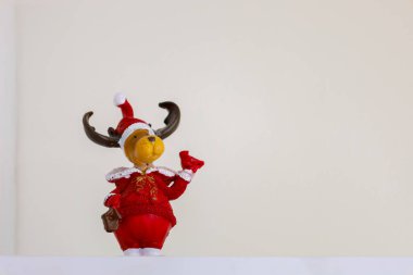 A small figurine of a reindeer in a red Santa Claus costume stands on a white background. The reindeer has brown fur, large antlers, and a red cap with a white pompom. clipart