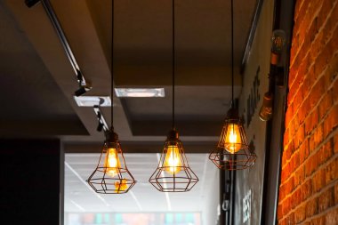 Fotoğraf, tavan arası tarzı elementlerle dolu bir odada sıcak ve rahat bir atmosfer oluşturan üç kolye ışığını gösteriyor..