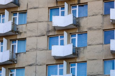 Bu fotoğraf, balkonları ve pencereleri olan bir apartmanın ön cephesini çekiyor. Binanın tipik Sovyet dönemi gri beton dokusu var..