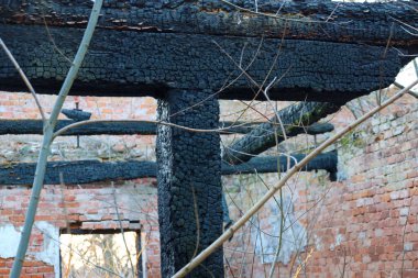 Fotoğraf yanmış bir binanın kalıntılarını gösteriyor. Tahta kirişler siyah, kömürleşmiş. Tuğla duvarlar yok edildi. Harabelerin arasında dallar büyür. Fotoğrafta yıkım kavramı anlatılıyor..