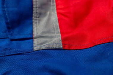 Mavi, kırmızı ve gri renklerin kombinasyonuyla kumaşın yakın çekim dokusu. Resim kumaşın dokusunu ve detaylarını vurgulayan dikişleri ve kıvrımları gösterir.