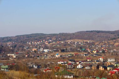 Fotoğraf, tepeler arasındaki bir vadide bulunan küçük bir kasabanın panoramik bir görüntüsünü yakalıyor. Kasaba evlerinin çeşitli renkleri ve mimari tarzları var..