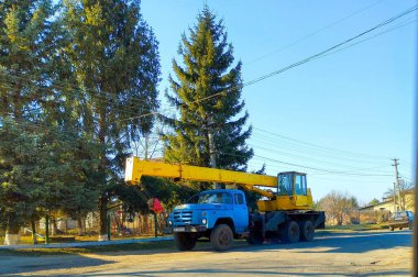Sambir, Ukrayna, - 10 Şubat 2025: Fotoğrafta kırsal bir alanda yolun kenarına park edilmiş sarı bir vinç olan mavi bir kamyon görülüyor.