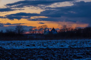 Canlı bir günbatımına karşı bir kilisenin siluetiyle büyüleyici bir kış akşamı manzarası..