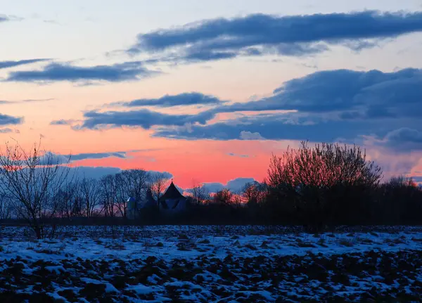 Kara bulutlar parlak gökyüzü ile çarpıcı bir tezat oluştururken ağaçların siluetleri ve ufuktaki bir bina derinlik ve gizem ekler..