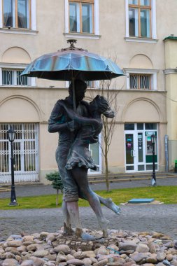 Drogobitch, Ukrayna, - 25 Mart 2025: Şemsiye altında romantik bir çiftin fotoğrafı, kemerli pencereleri olan bir binanın arka planında, bir parkta..