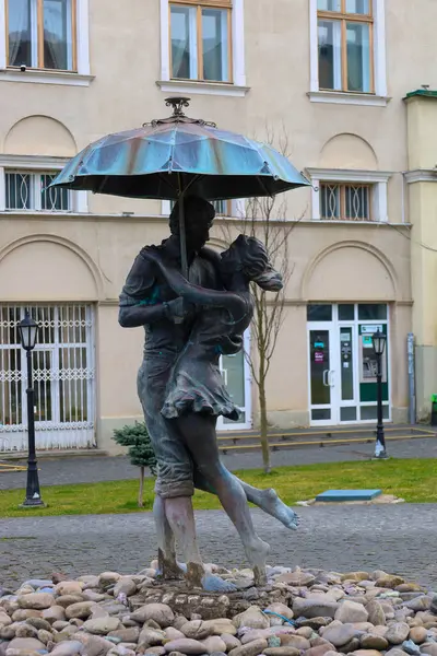 Drogobitch, Ukrayna, - 25 Mart 2025: Şemsiye altında romantik bir çiftin fotoğrafı, kemerli pencereleri olan bir binanın arka planında, bir parkta..