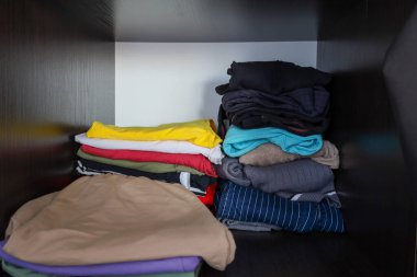 Fotoğrafta bir dolapta katlanmış giysiler var. Giysiler düzgünce katlanmış, organize depolamayı gösteriyor. Dolapta elbise depolamak için kullanılan raflar var..