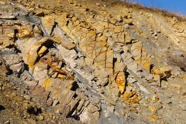 Çeşitli katmanları ve renkleri olan bir kaya oluşumunun yakın çekimi. Gri, sarı ve kahverengi renkli katmanlar görülebilir. Kayaların farklı doku ve şekilleri var..